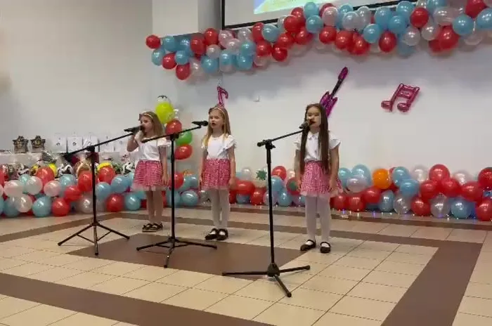 Trzy uczennice z oddziału przedszkolnego śpiewają do mikrofonów